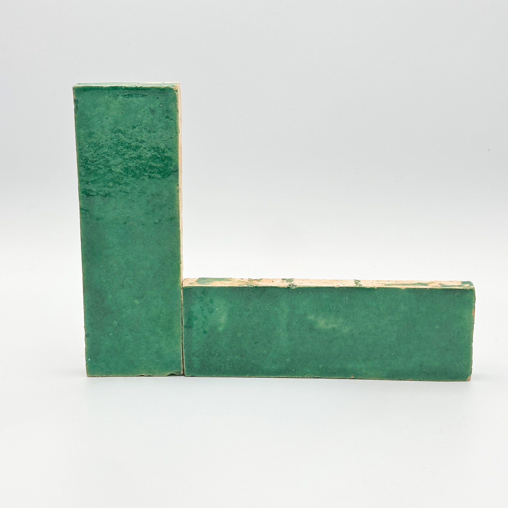 Montage en équerre de deux bejmats émaillés verts, mettant en relief l'épaisseur de la terre cuite artisanale et la brillance de l'émail.