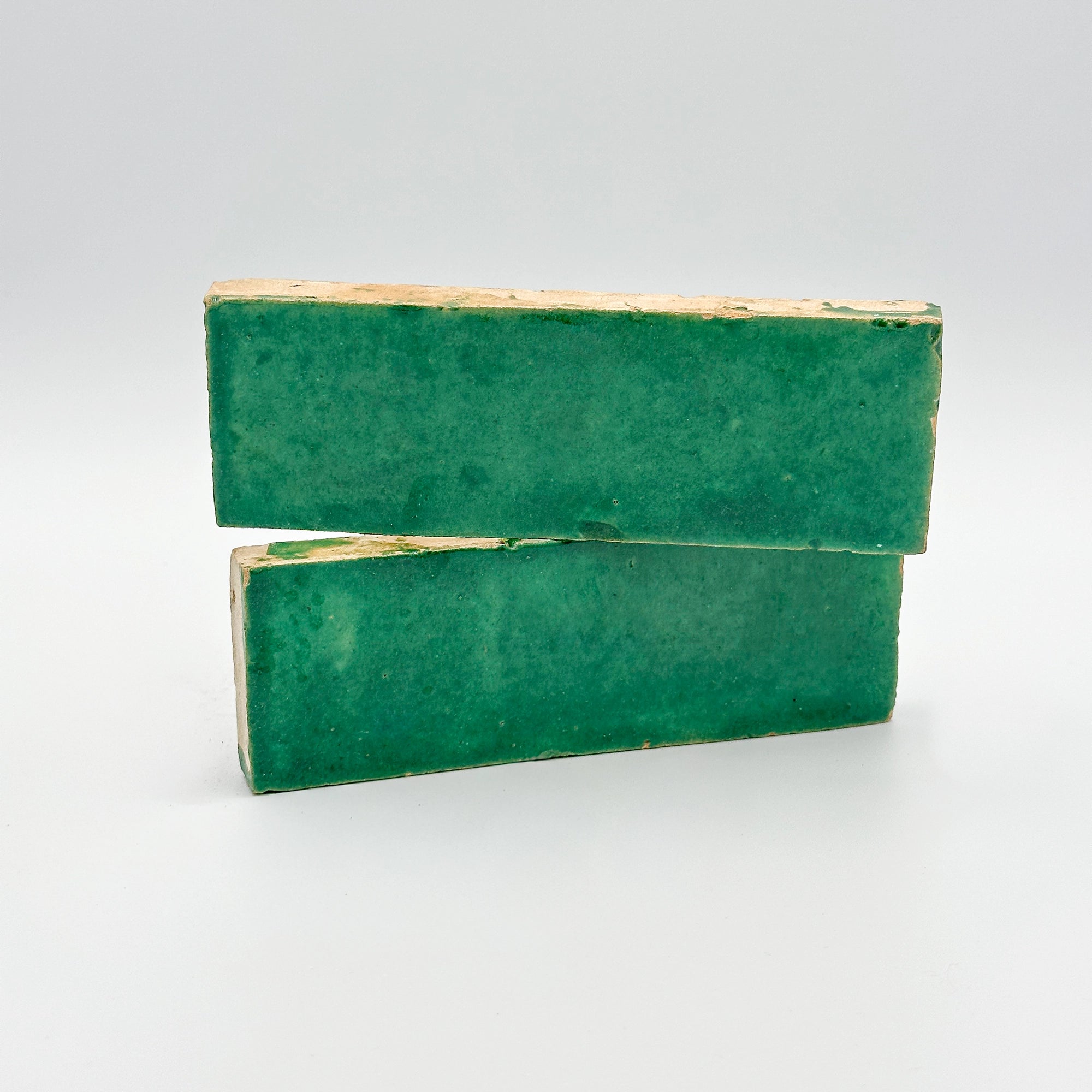 Carreau de bejmat émaillé vert posé à la verticale, révélant la brillance de l'émail et ses bords irréguliers en terre cuite.