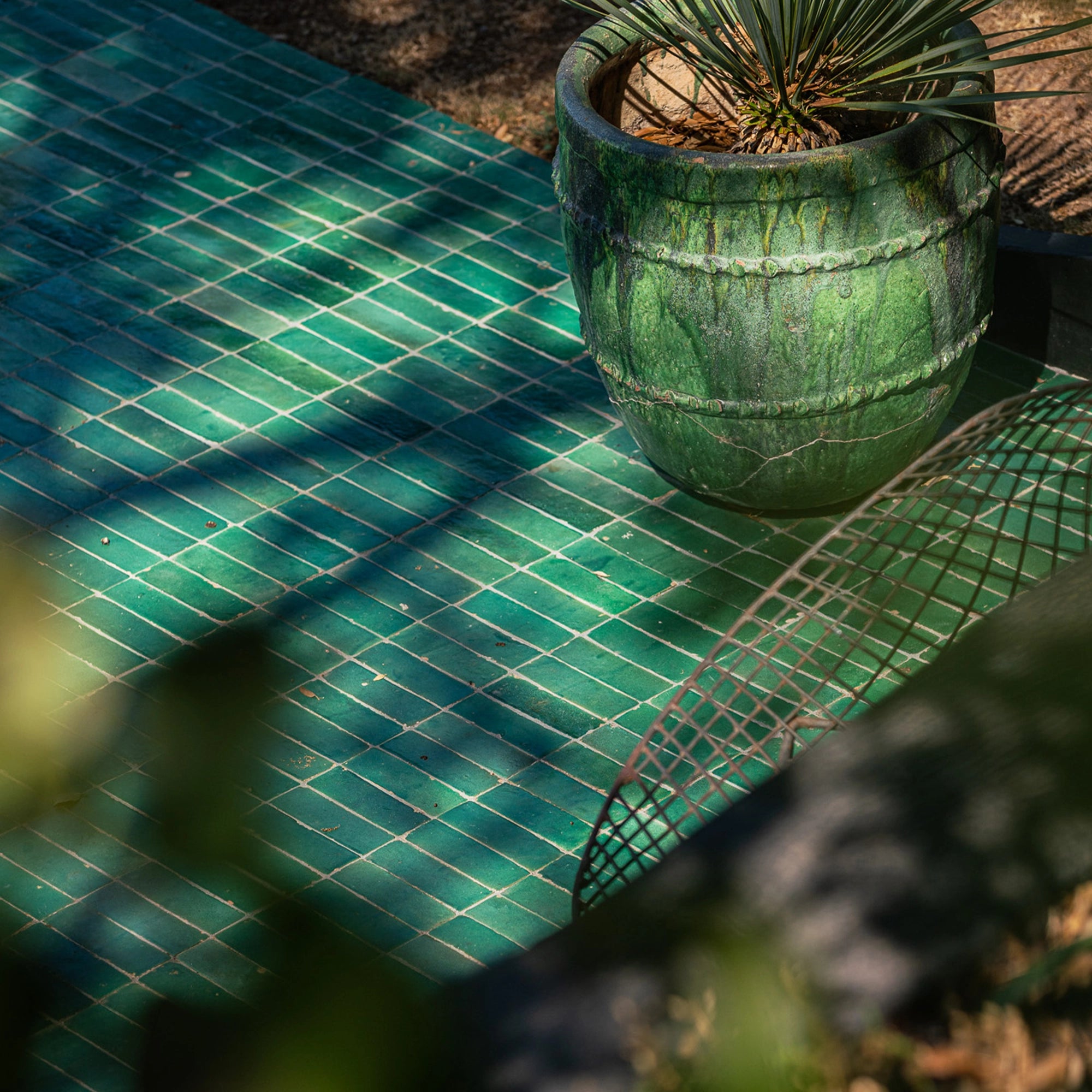 Gros plan sur un bejmat émaillé vert posé à la verticale, révélant les bords irréguliers et la brillance de l'émail artisanal.